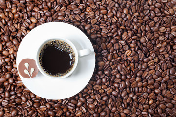 top view of a cup of black coffee and a piece of chocolate on a white plate placed on coffee bean background,copy space. Clipping path included.