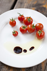 Cherry tomatoes with olive oil and balsamic vinegar on a white plate, focus on foreground.