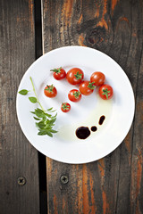 Cherry tomatoes with fresh basil, olive oil and balsamic vinegar on a white plate, top view. Copy space.