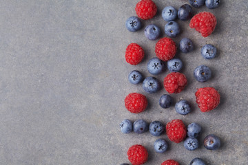 Blueberries and raspberries in a bowl on rusty grey background. Top view