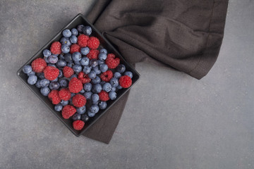 Blueberries and raspberries in a bowl on rusty grey background. Top view