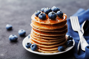 Pile de crêpes ou de beignets américains cuits au four avec des myrtilles et du sirop de miel sur une table noire rustique. Dessert délicieux pour le petit déjeuner.