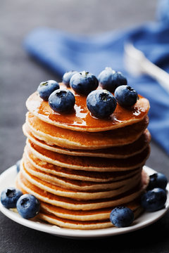 Stack of baked american pancakes or fritters with blueberries and honey syrup on rustic dark table. Delicious dessert for breakfast.