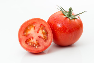 One whole tomato and one sliced tomato on a white background.