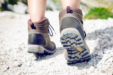 Woman hiker walk on a rocky ground.  Sunny day.Trekking boots.Lens flare. Succesful backpacker. Stone. Step