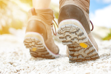 Woman hiker walk on a rocky ground.  Sunny day.Trekking boots.Lens flare. Succesful backpacker. Stone. Step