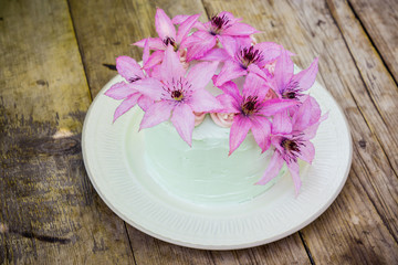 Creamy cake with clematis flowers on the wooden table. Shallow depth of field.