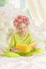 little girl in hair curlers with book