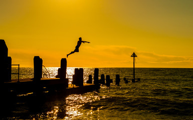 Aberystwyth, West Wales, Sunday 22 May 2016 UK Weather: A day that started out cloudy ended in clear skies and sunshine. A young student jumps from the wooden jetty at sunset.