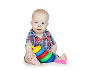 Baby boy in checkered shirt sits and plays with multi-colored pyramid