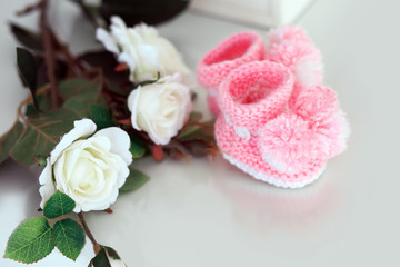 Pink baby booties on a table with white roses.