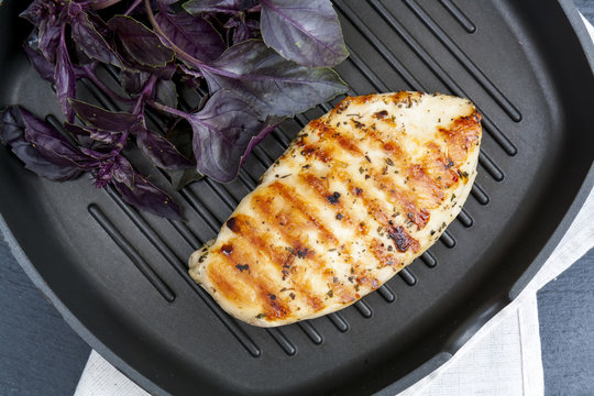 Grilled chicken breast steak with violet basil on teflon pan grill, black slate stone background, top view