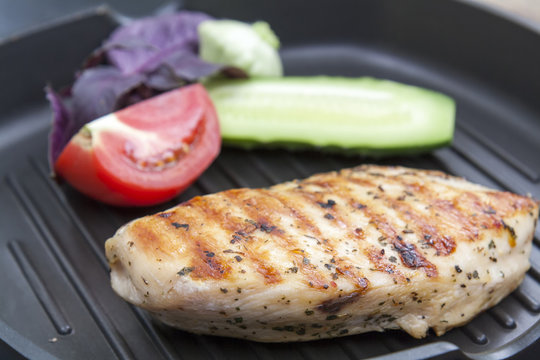Grilled chicken breast steak with tomato, cucumber and violet basil on teflon pan grill, black slate stone background