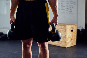 Closeup of athlete holding two kettlebells weights at the gym