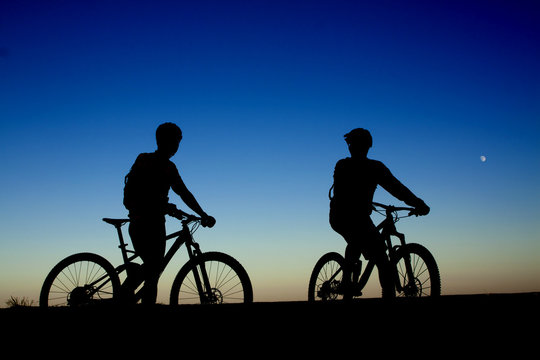 Two cyclists on the background of night sky and moon