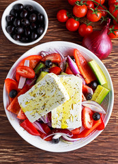 Greek salad with fresh sweet pepper, red onion, orange cherry tomatoes, cucumber, black olives and feta chees drizzled extra virgin olive oil on wooden table