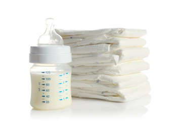 Baby bottle with milk and pile of diapers isolated on white