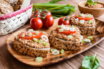 Whole wheat bread slices with sardine spread, tomato and green onion on a wooden background