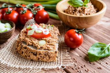 Whole wheat bread slices with sardine spread, tomato and green onion on a wooden background