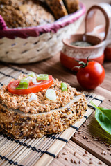 Whole wheat bread slices with sardine spread, tomato and green onion on a wooden background