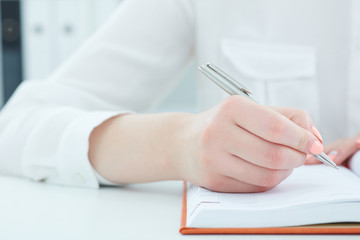 Female hands holding a silver pen and making notes closeup. Business job offer, financial success, certified public accountant concept.