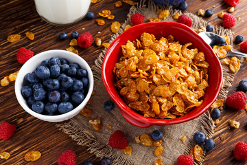 Corn Flakes with berries raspberries, blueberries, glass of milk, and sweet honey.