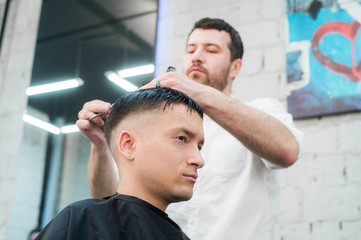 Fototapeta premium Professional styling. Close up side view of young man getting haircut by hairdresser with electric razor at barbershop