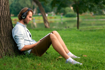 Student with headphones in park of campus read a book