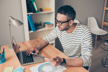 Concentrated smart worker in glasses with tablet typing on lapto