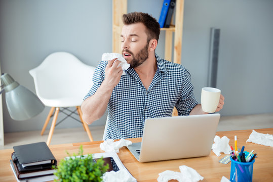 Sick businessman holding cup of hot tea and sneezing in tissue