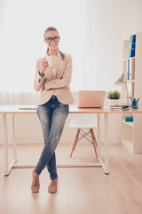 Happy businesswoman standing near her working place and drinking