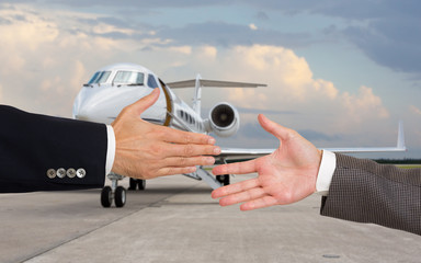Businessmen about to shake hands in front of corporate jet. Focus on hands