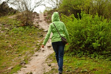 Девушка в зеленой куртке идет в гору под дождем