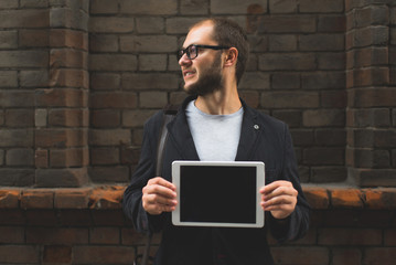 young guy with the tablet against the wall, holding technology