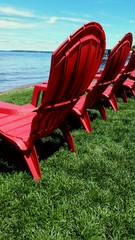Red adirondack chairs in the grass on the beach waterfront