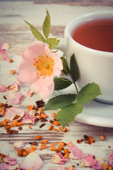 Vintage photo, Cup of tea with wild rose flower on old rustic wooden background