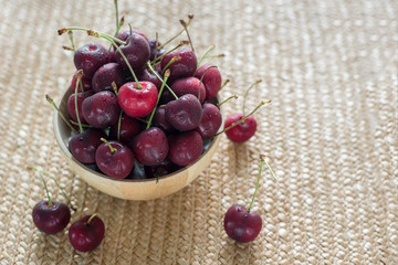 Cherries with water drops in wooden bowl on natural weaving
