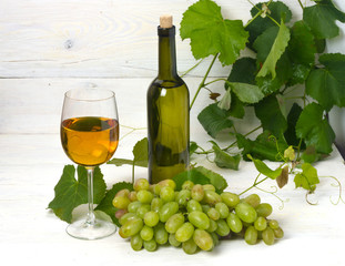 glass and bottle of white wine with grapes on a wooden table