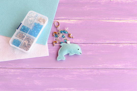 Hand cute felt dolphin keychain. Handbag charms. Handmade car keyring. Set of beads in a plastic box, felt sheets on lilac wooden background with free place for text. Summer crafts for kids concept