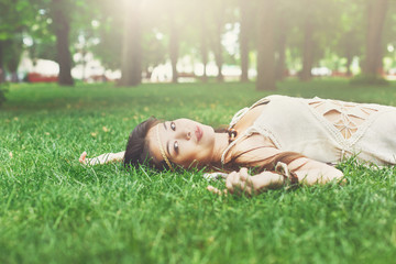 Beautiful young girl lying on grass in summer park