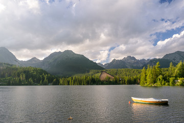 Obraz premium Peaceful mountain scene with mountain hotel next to a lake with boat. Scenic view of Strbske Pleso, High Tatras National Park, Slovakia.