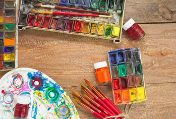 Fototapeta premium Watercolor paints, brushes and palette on wooden background. The workplace of the artist. Banner for school