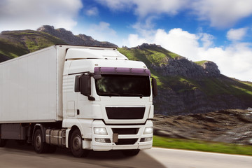 LKW fährt auf einer Landstraße mit Gebirge im Hintergrund
