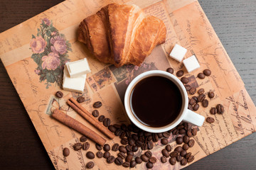Cup of coffee, croissant, coffee grains, cinnamon and sugar