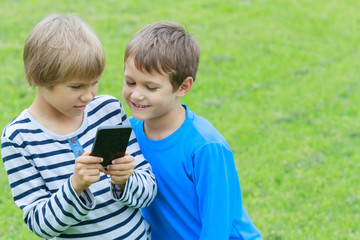 Children with smartphone. Two boys looking to screen, playing games or using application. Outdoor. Technology education leisure people friendship concept