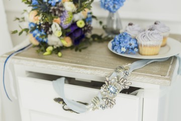 Fototapeta na wymiar Wedding decorations with bride's bouquet, candle and cupcakes. blue and serenity, focus on blue bride's belt