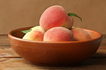 Ripe peaches with leaves in bowl on a brown wooden background