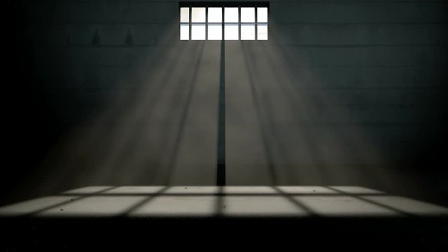 A slow pan out of a days time-lapse of an empty dark jail cell with light rays penetrating a barred window casting a shape on the floor