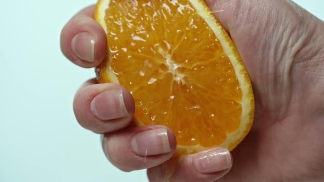 Extreme close up shot of hand squeezing half of fresh ripe orange and juice bursting out and dripping over fingers on white background in slow motion