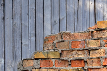 Fragment of destroyed brick wall on the background wall of wood.